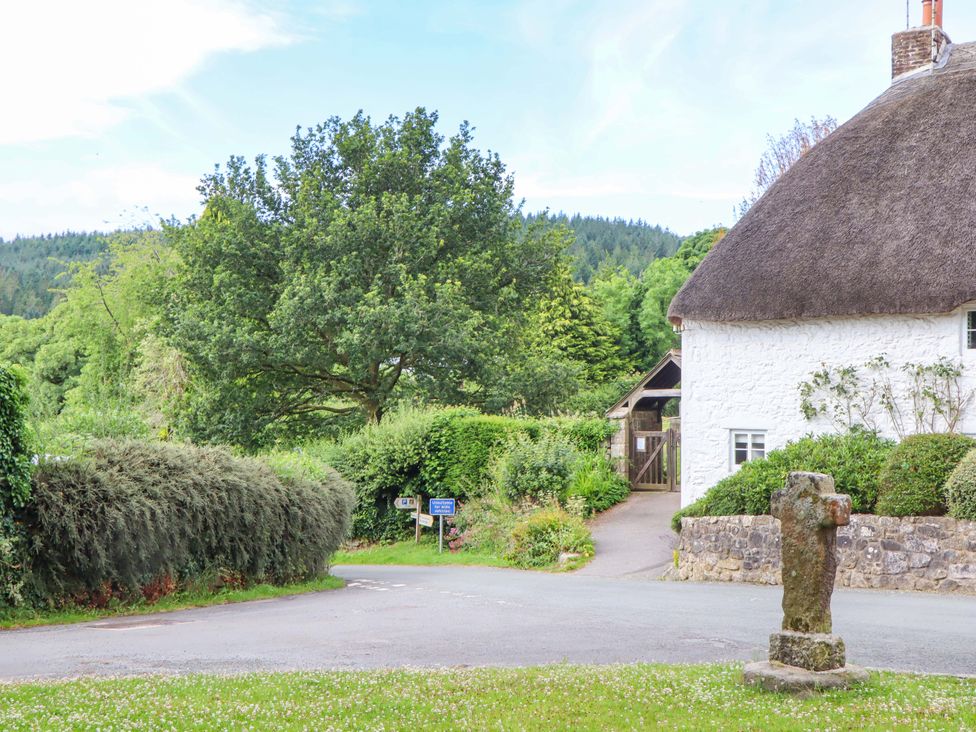 A cottage with a thatched roof and stone cross at Little Gate Cottage in North Bovey