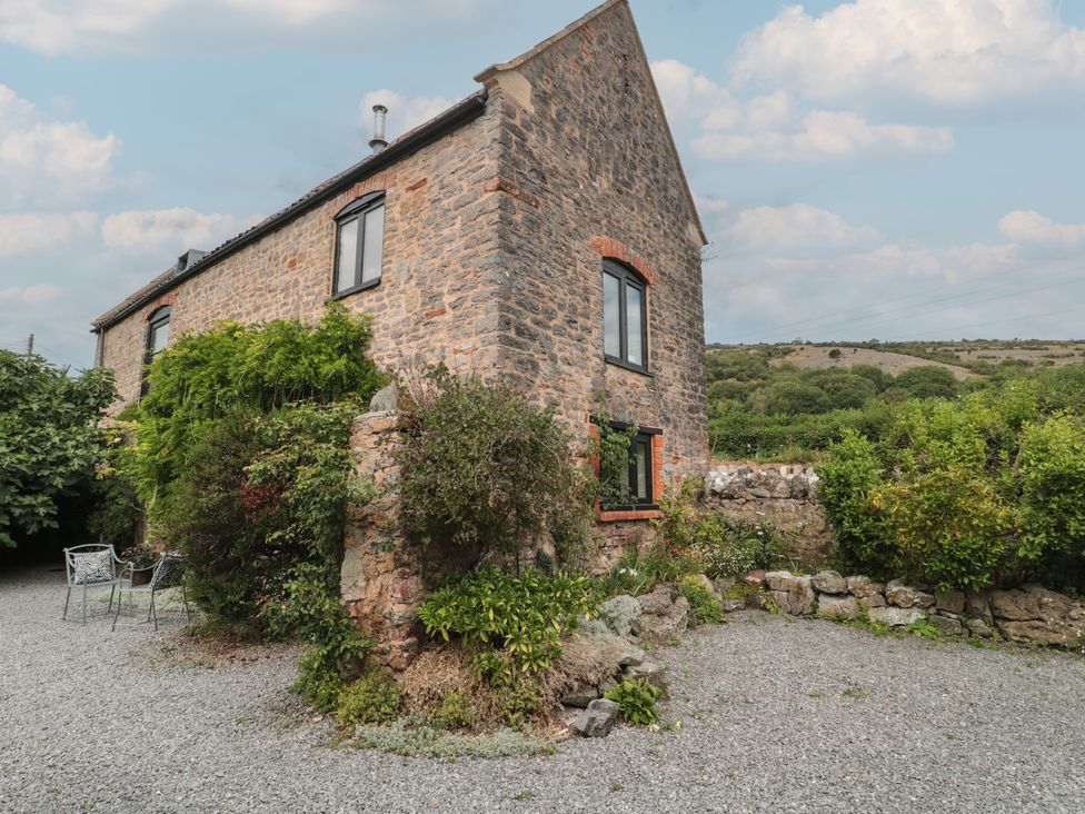 A stone building with windows and a seating area in a garden at The Barn in Compton Bishop near Cheddar