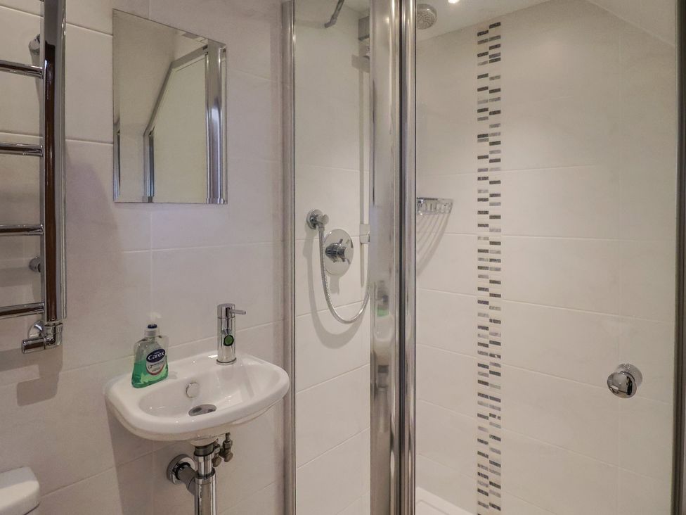 A bathroom with a shower, hand basin, and towel rail at The Old Log Shed in Honiton