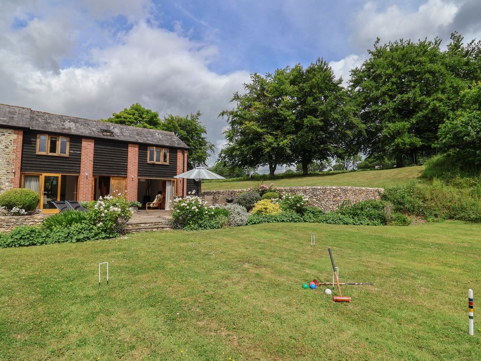 An outdoor view of a garden with a house and croquet set at The Old Log Shed in Honiton
