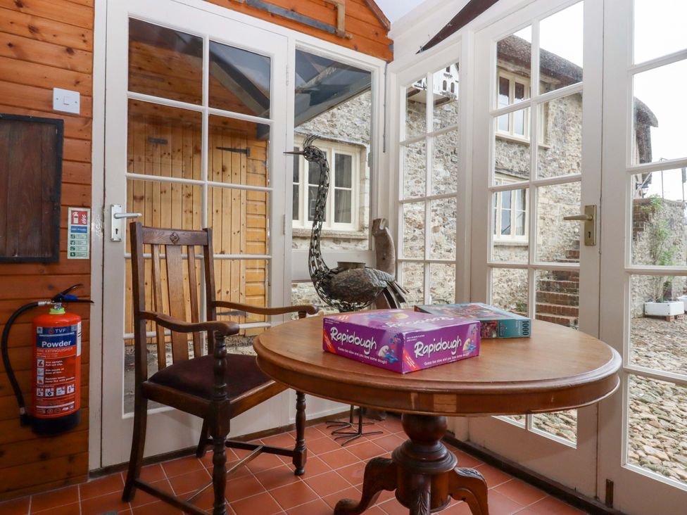 A conservatory with a table, chair, board games and a statue at Hornshayne Farmhouse Farway, near Honiton