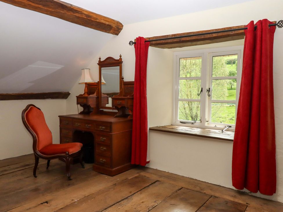 A bedroom with a chair and a vanity with mirror at Hornshayne Farmhouse near Honiton
