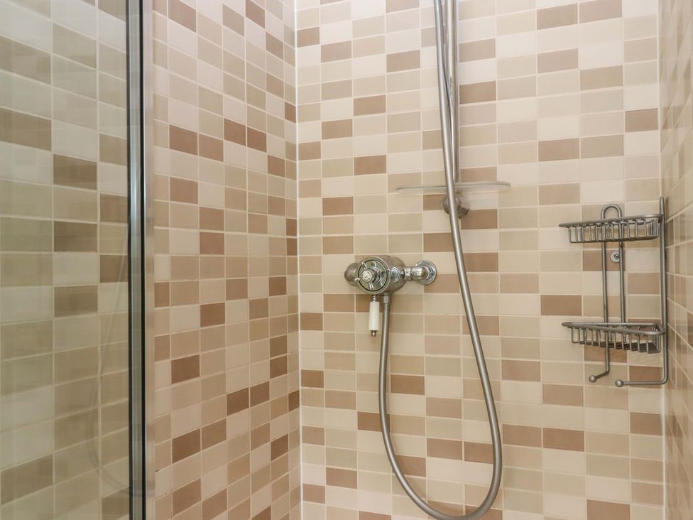 A shower with tiled walls and shower fixtures at Hornshayne Farmhouse in Farway, near Honiton