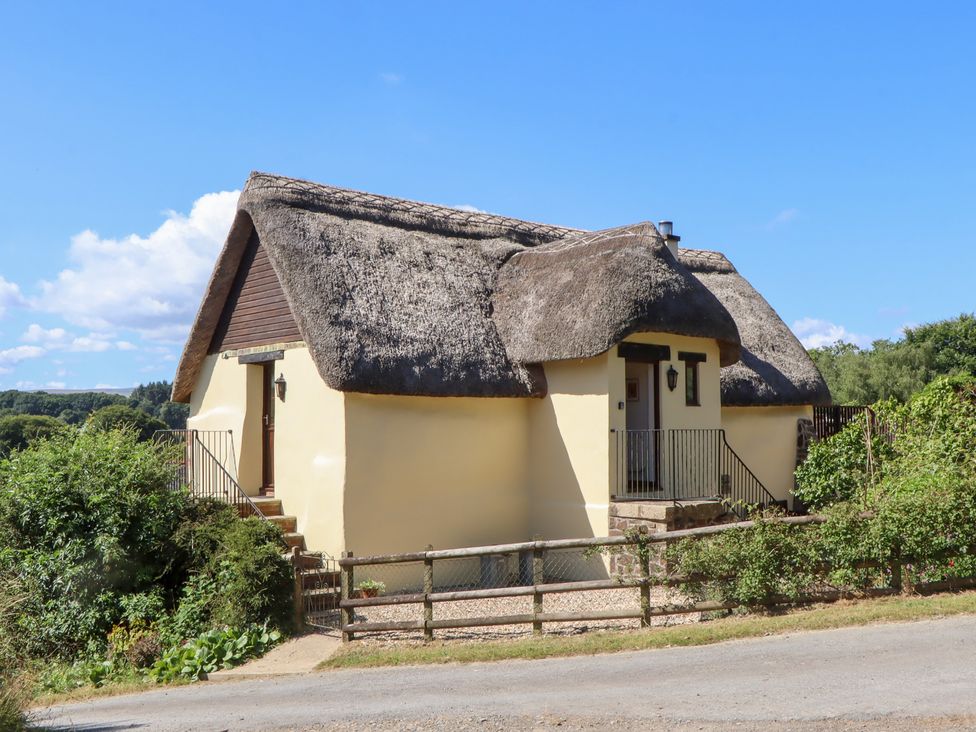 A cottage with a thatched roof and steps leading to the front door at The Cottage in Sampford Courtenay