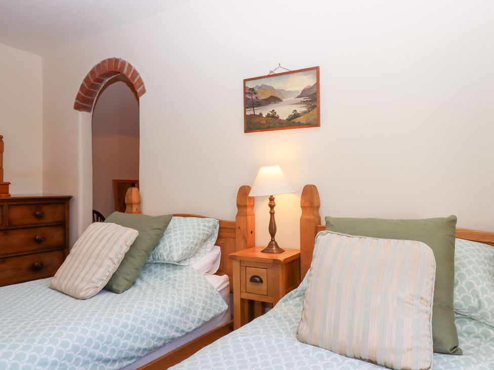 A bedroom with two beds and a lamp on a nightstand at The Cottage in Sampford Courtenay