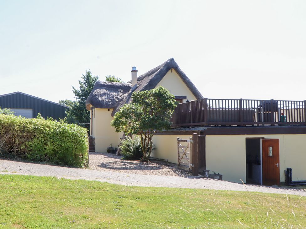 A thatched roof house with a deck and garden at The Cottage in Sampford Courtenay