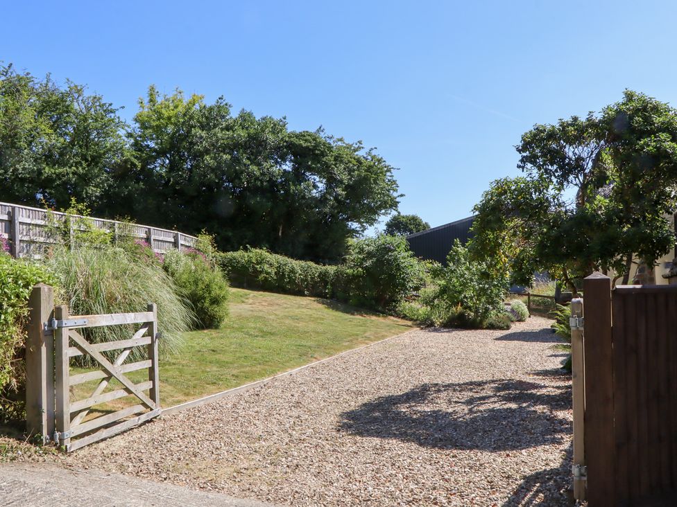 A gravel driveway with a gate and trees at The Cottage in Sampford Courtenay