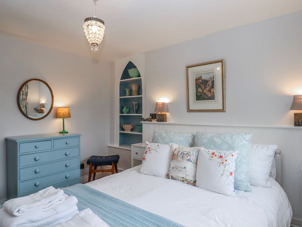 A bedroom with a bed, nightstands, and decorative items at Chapel Cottage in Welcombe
