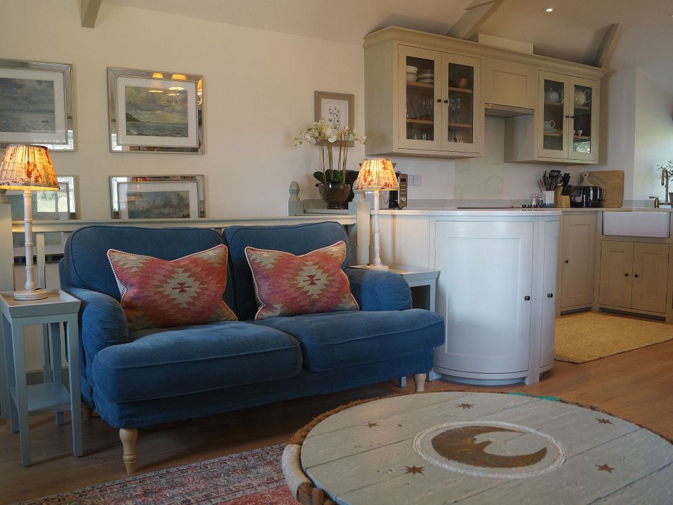 A living room with a sofa and kitchen area at Coach House Cottage, Strete, near Dartmouth