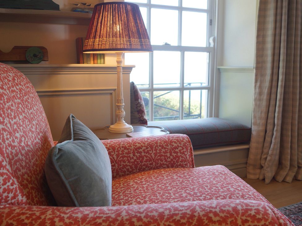 A living room with an armchair, lamp, and window at Coach House Cottage in Strete, near Dartmouth