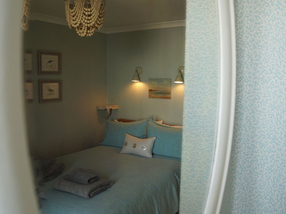 A bedroom with a bed and framed paintings at Coach House Cottage, Strete, near Dartmouth