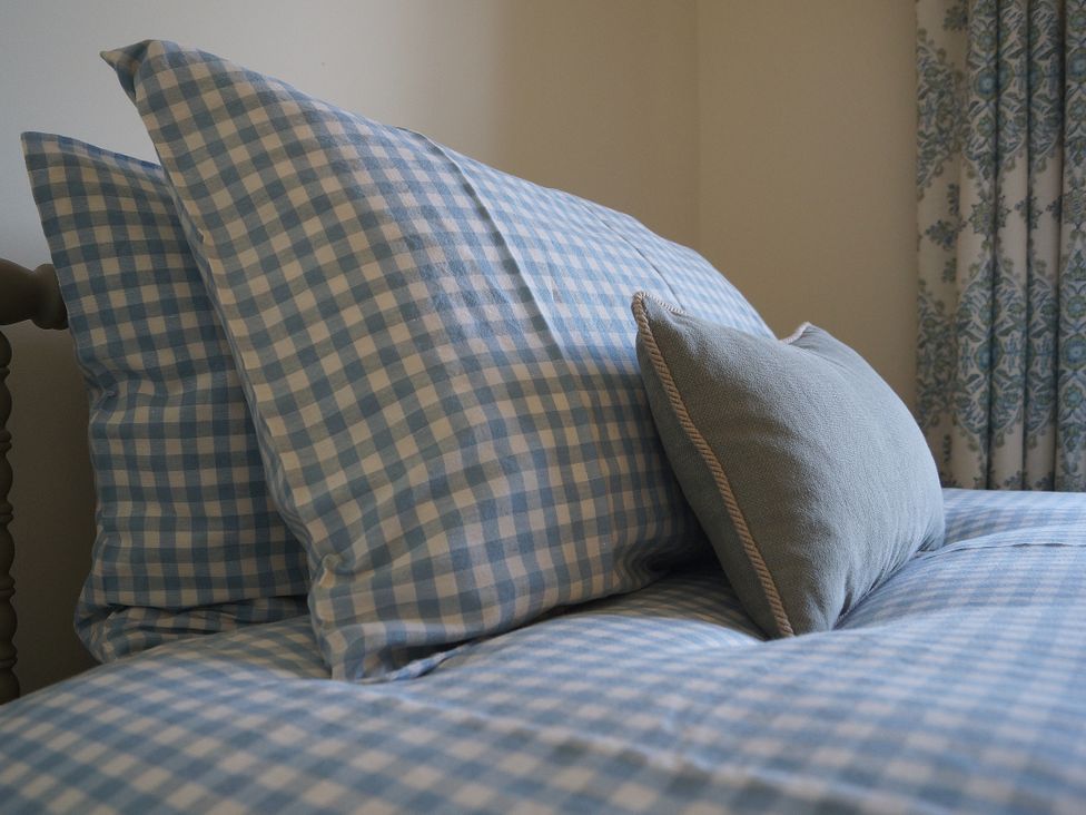 A bed with blue checkered pillows in Coach House Cottage Strete, near Dartmouth