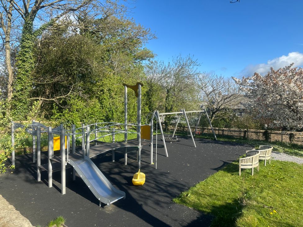 A playground with slide and swings surrounded by grass at The Hay Barn in Halwell