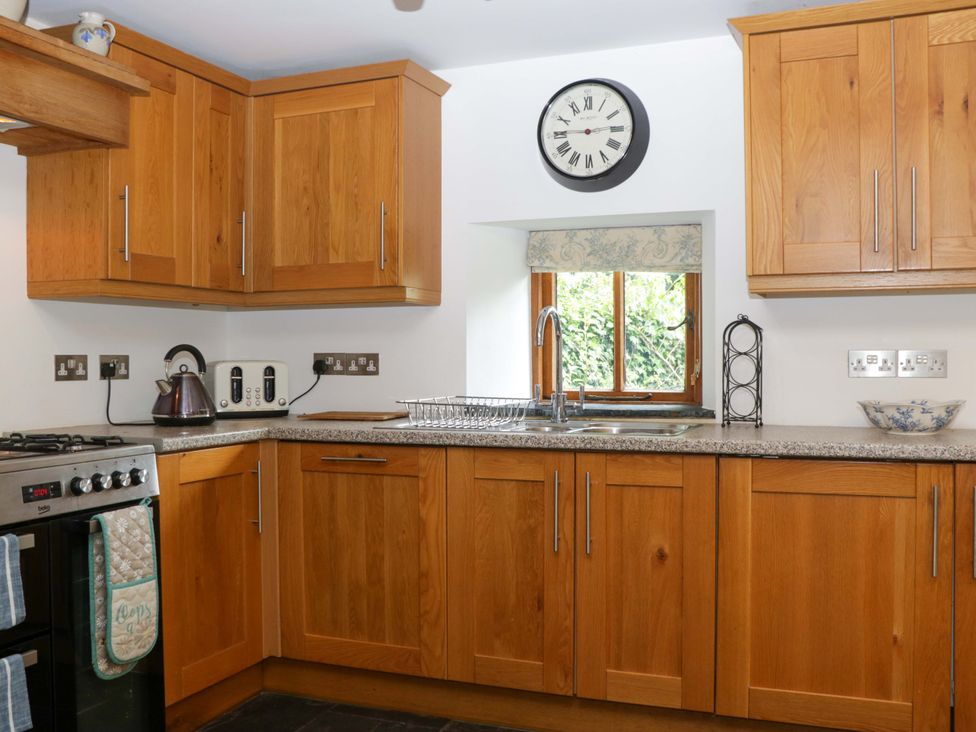 A kitchen with wooden cabinets and a sink at The Hay Barn in Halwell
