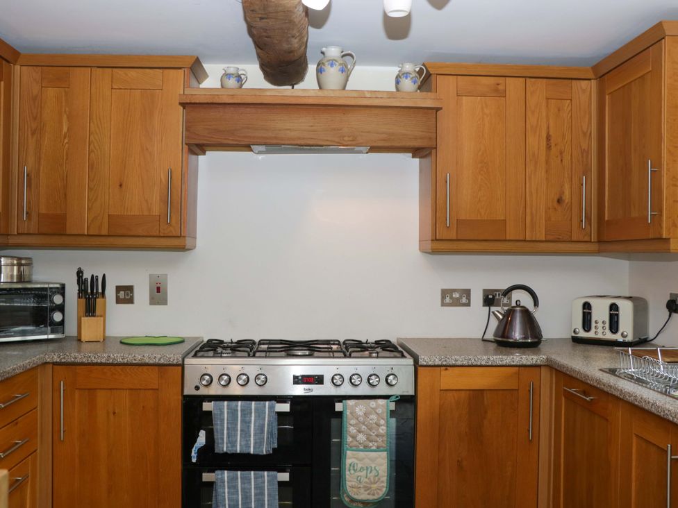 A kitchen with appliances and wooden cabinets at The Hay Barn in Halwell