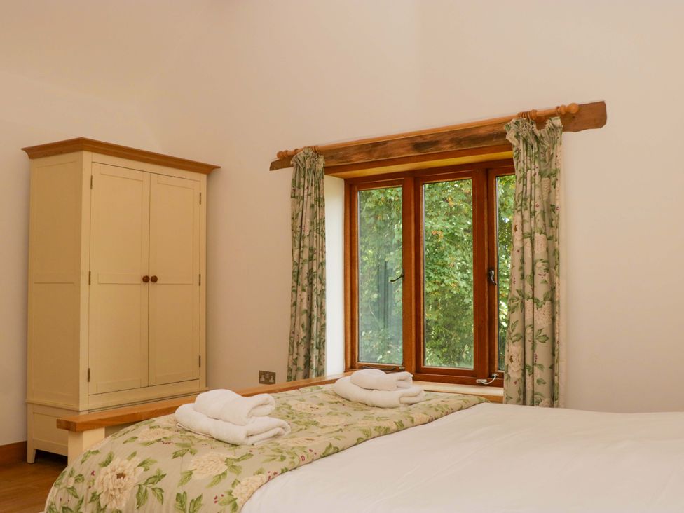 A bedroom with a bed, wardrobe, and window at The Hay Barn in Halwell