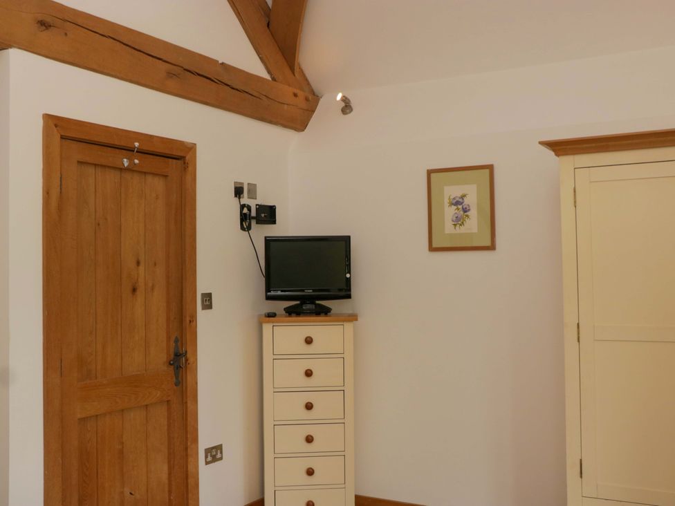 A bedroom with a door, television, and drawers at The Hay Barn Halwell