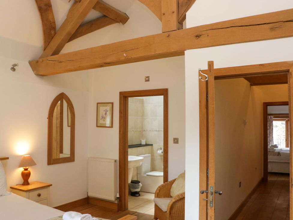 A bedroom with a bed, lamp, and bathroom access at The Hay Barn in Halwell