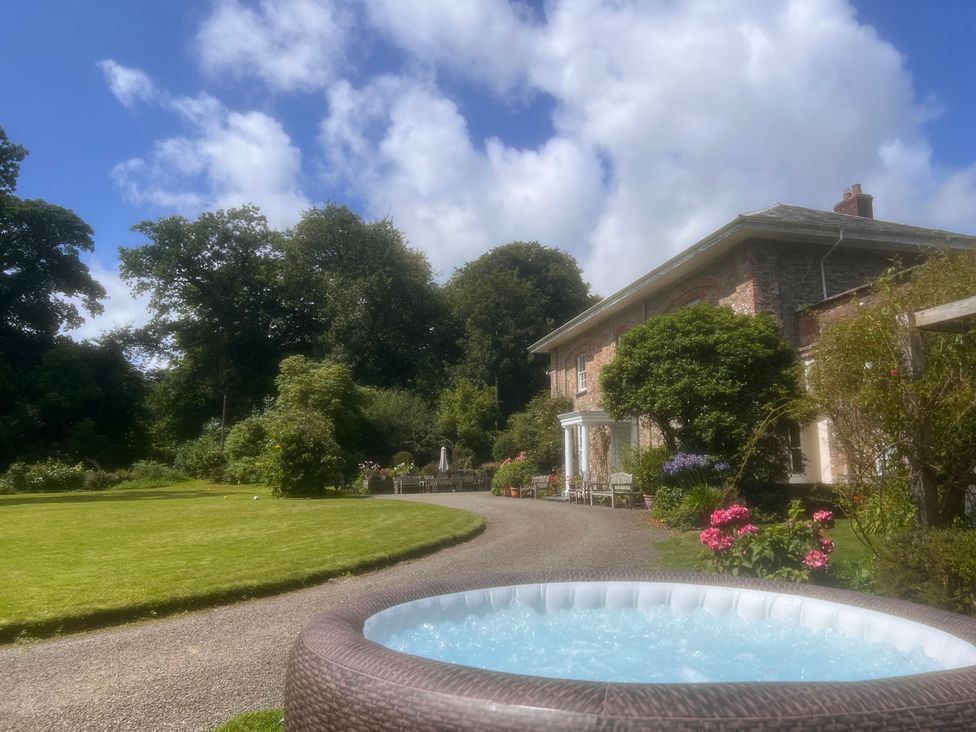 A hot tub in the garden with a house and trees at Parnacott in Holsworthy
