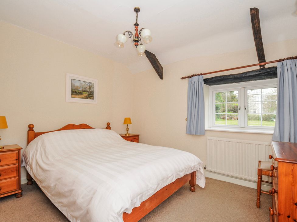 A bedroom with a bed, nightstand, and window at Tumrose Cottage in Blisland