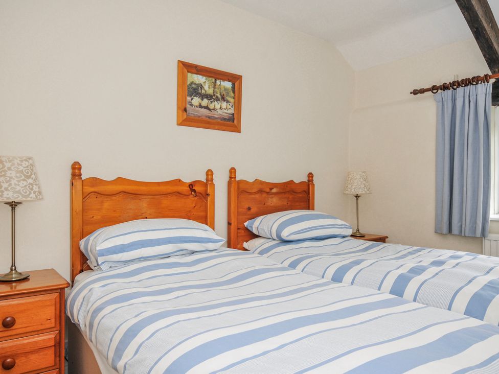 A bedroom with two beds, bedside table, and lamp at Tumrose Cottage in Blisland
