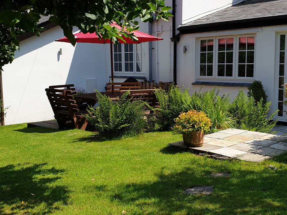 A garden with a table and chairs under a parasol at Orchard Lodge in Boscastle