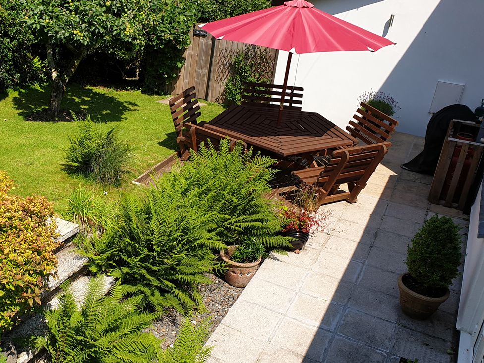 A garden with a wooden table and chairs under an umbrella at Orchard Lodge Boscastle