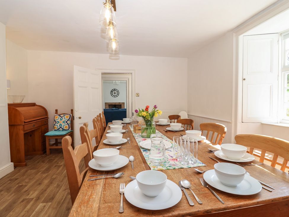 A dining room with a long wooden table set for a meal at Tregonhawke Farmhouse in Millbrook