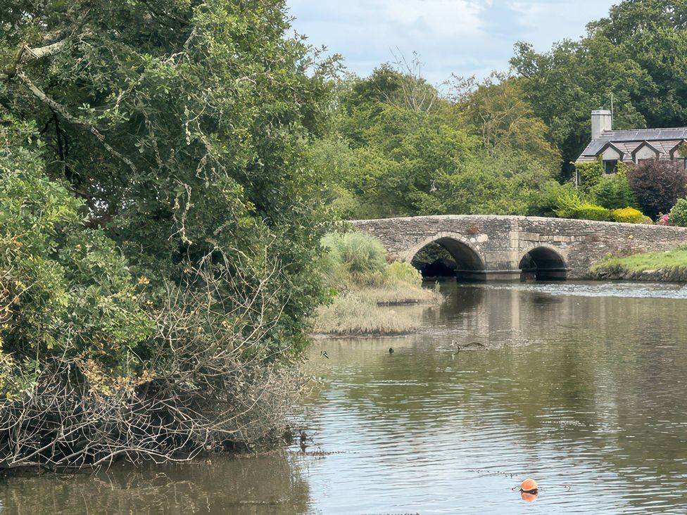 A view of a bridge over water surrounded by trees and a house at Kingbarth in Lerryn