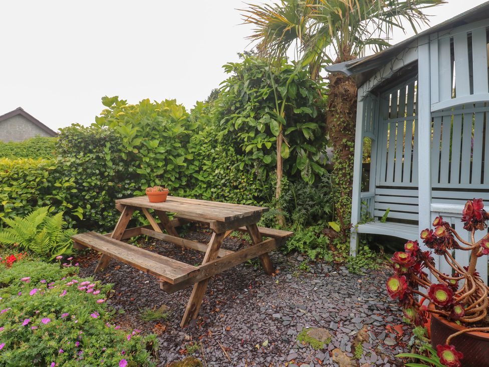 A garden with a wooden table and bench surrounded by plants at 2 The Cottages Ludgvan