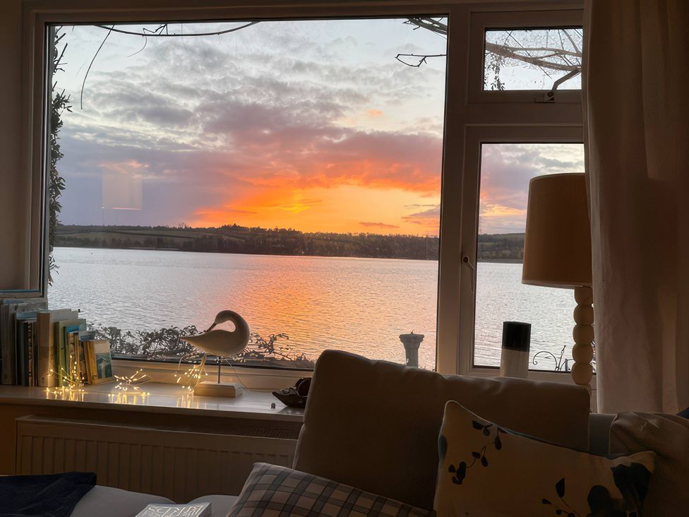 A living room with a view of a sunset over water at Clamoak Cottage near Bere Alston