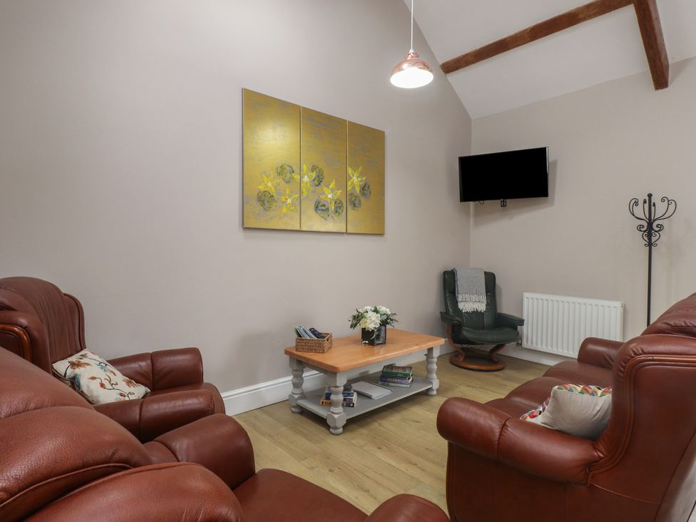 A living room with leather furniture and a television at Coetsiws in Clynnog Fawr