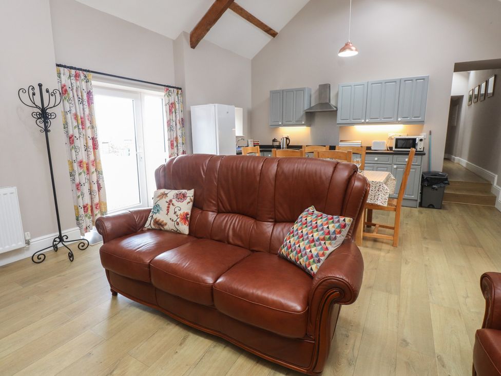 A living room with a brown sofa and kitchen area at Coetsiws in Clynnog Fawr