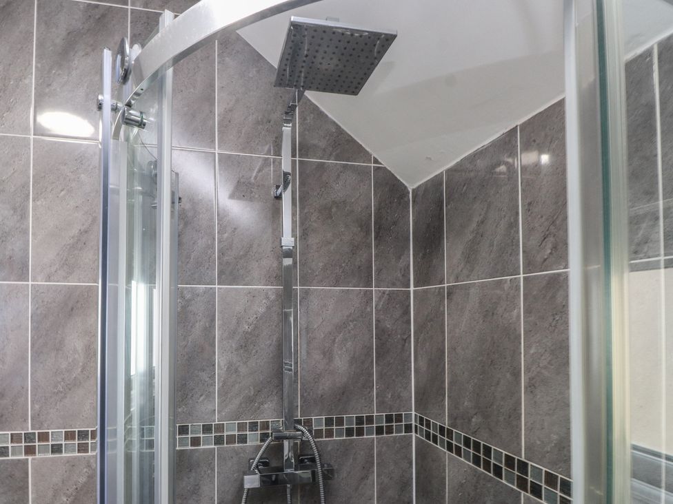 A shower with a glass enclosure and tiled walls at Coetsiws in Clynnog Fawr