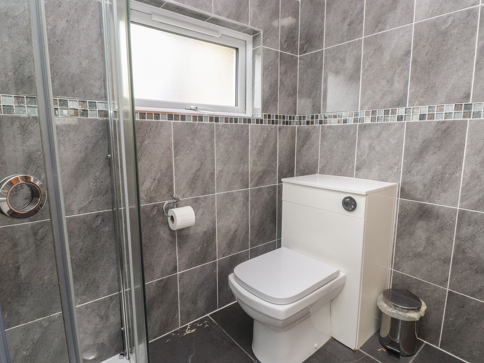 A bathroom with a shower, toilet, and waste bin at Coetsiws in Clynnog Fawr
