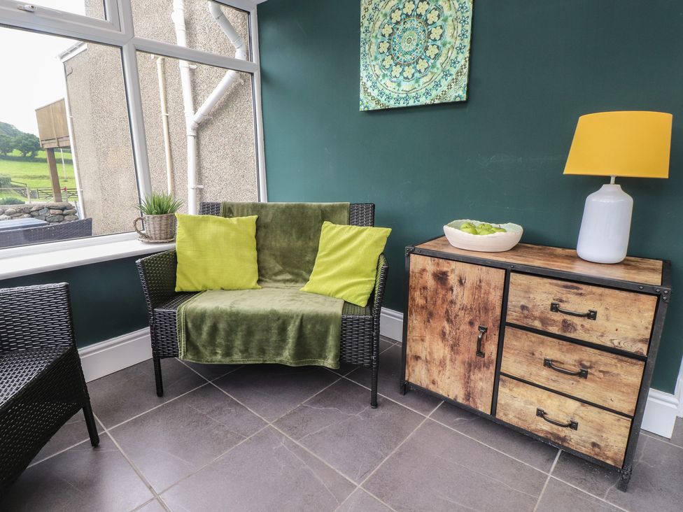 A snug with a chair and a wooden cabinet at Coetsiws in Clynnog Fawr