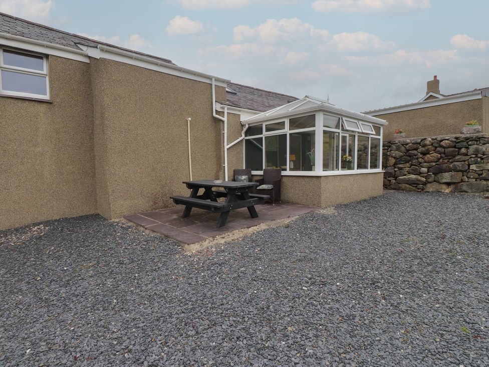 A garden with a conservatory and dining table at Coetsiws in Clynnog Fawr