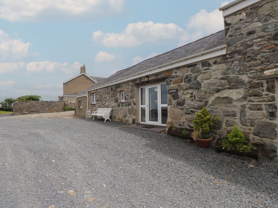 An exterior view of a stone building with a bench and potted plants at Coetsiws Clynnog Fawr