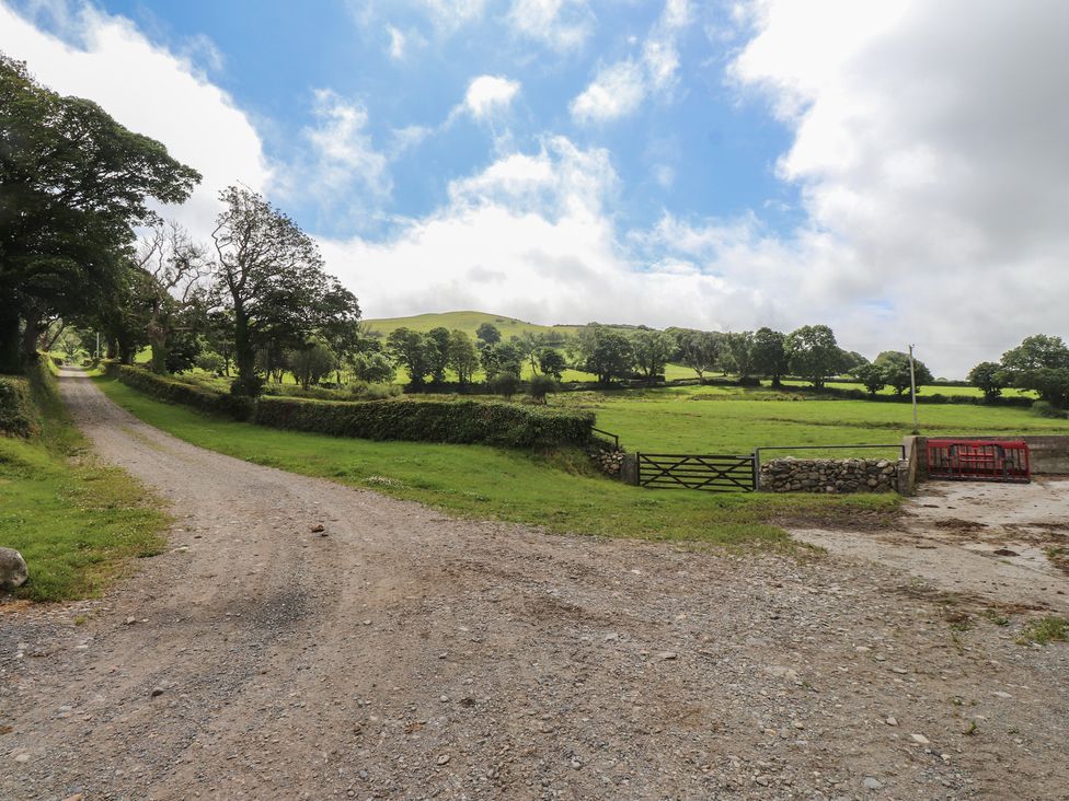 A gravel road leading to a gate with fields and trees at Coetsiws Clynnog Fawr
