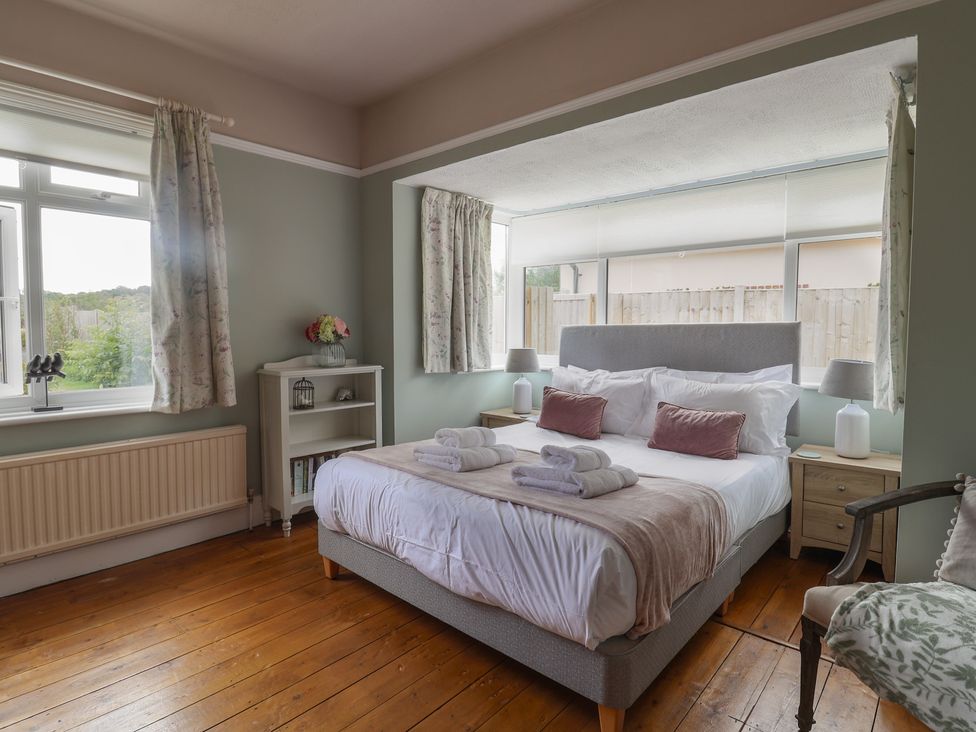 A bedroom with a bed, nightstand, and windows at Sunny Croft in Broadmayne near Dorchester