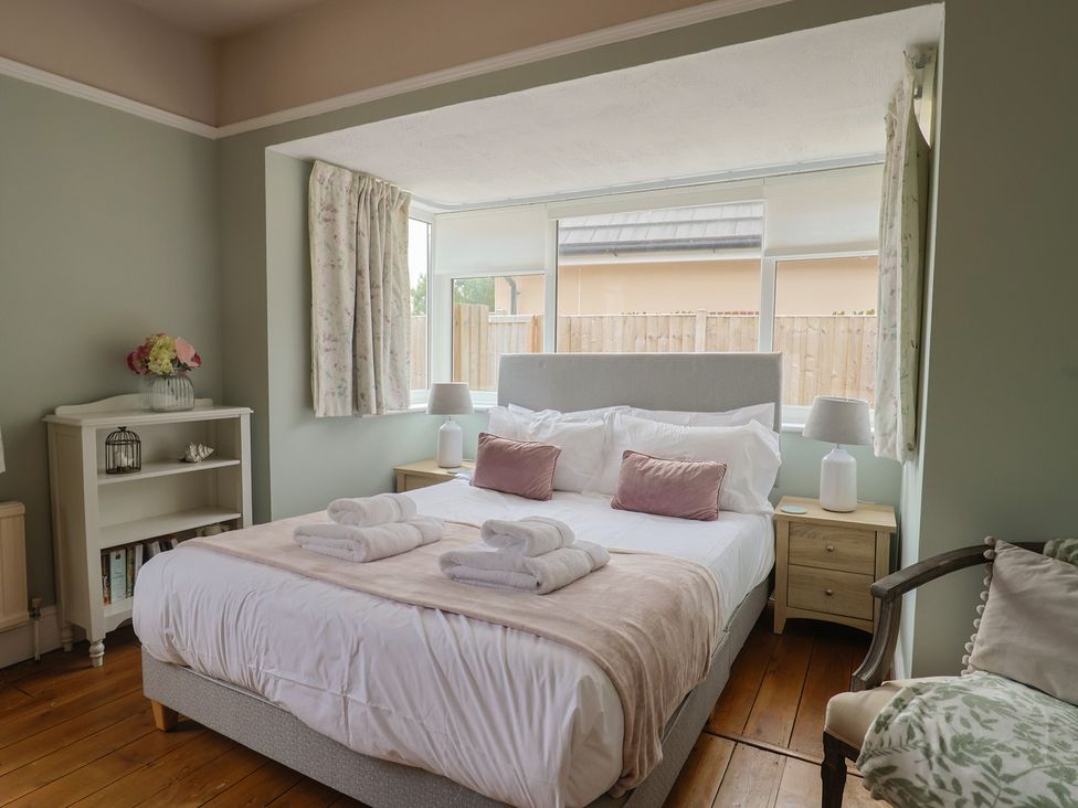 A bedroom with a bed, nightstands, and windows at Sunny Croft in Broadmayne near Dorchester