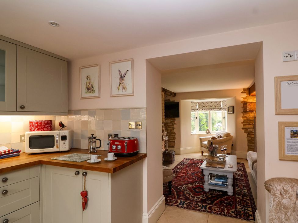 A kitchen with appliances and a view into the living room at Puffitts Cottage in Bourton-on-the-Water