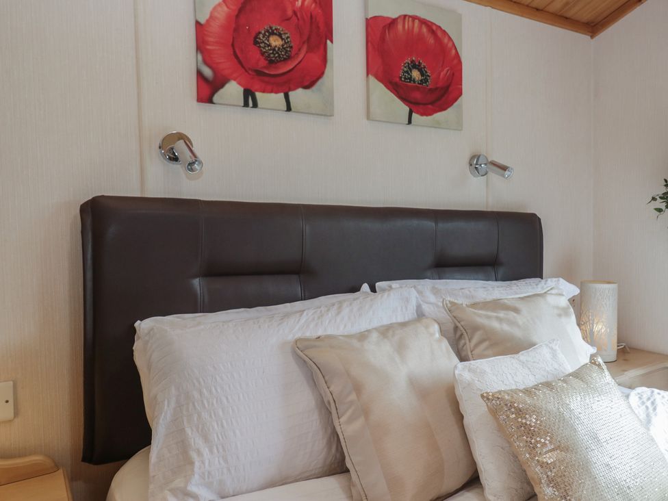 A bedroom with a bed, pillows, and wall art at The Cedars in South Lakeland Leisure Village