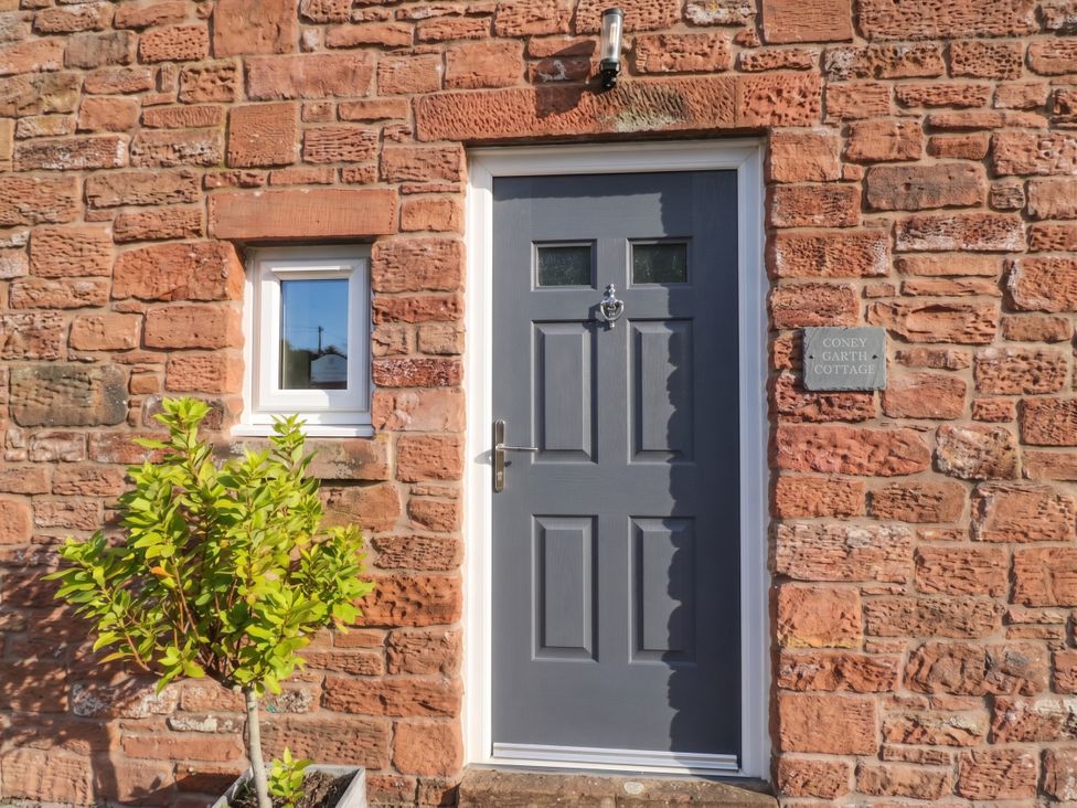 A door and window on a brick wall with a plant at Coney Garth Cottage in Beckermet