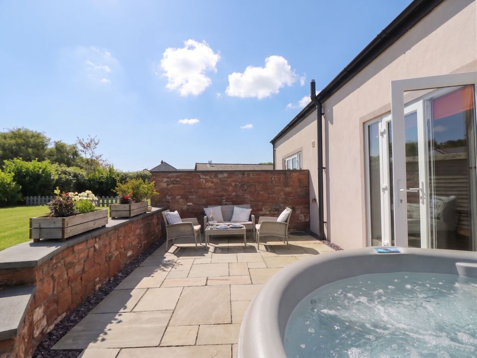 An outdoor area with a hot tub and seating at Coney Garth Cottage in Beckermet