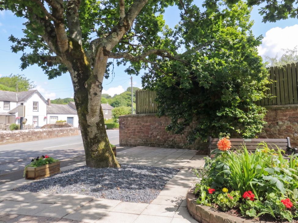 An outdoor area with a tree, bench, and flower bed at Coney Garth Cottage in Beckermet
