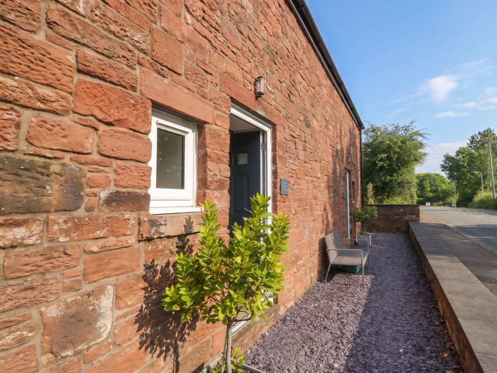 An exterior view of a property with a stone wall and a bench at Coney Garth Cottage Beckermet