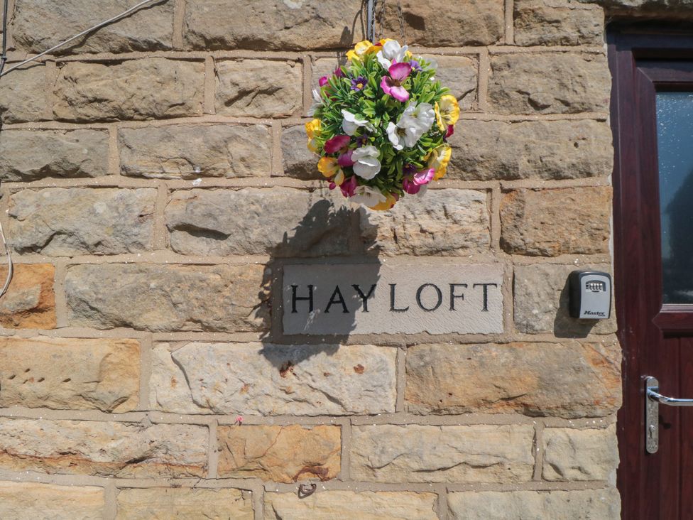 A stone wall with a flower basket and sign at Hayloft in Staintondale