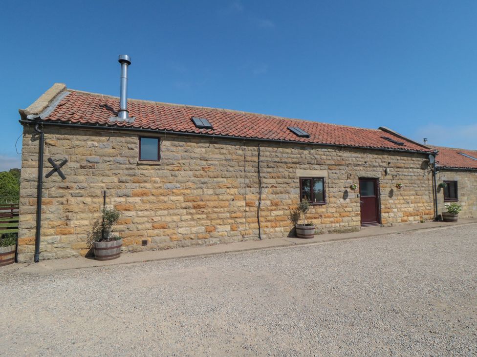 An exterior view of a building with a stone wall and a gravel driveway at Hayloft in Staintondale
