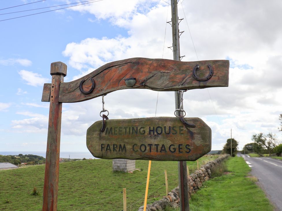 A sign indicating Meeting House Farm Cottages near a road at Hayloft in Staintondale